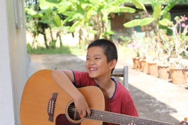 Neşeli bir çocuk, akustik gitarını açık havada çalmaktan zevk alır. Güzel bir doğal ortamda müzik için neşe ve tutku yayar..