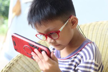 Gözlük takan genç bir çocuk evde rahat bir ortamda akıllı bir telefonla etkileşime giriyor. Sahne odak ve merakı yakalar.