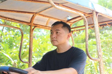 Odaklanmış bir adam yemyeşil bir arazide klasik bir traktör sürüyor, kırsal hayatın özünü somutlaştırıyor ve sakin bir çevrede açık hava macerası..