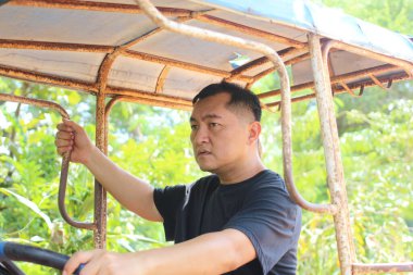 Odaklanmış bir adam yemyeşil bir alanda kırsal bir araç kullanıyor, doğal çevreyle bağlılık ve kararlılık gösteriyor. Kırsal yaşam ve tarım projeleri için ideal.