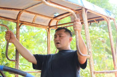 Bir adam lüks bir açık hava ortamında araç kullanırken dikkatle odaklanır. Duruşu ve ifadesi, görevdeki kararlılığını ve bağlılığını yansıtıyor..