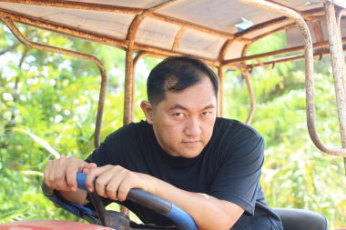 Ciddi bir adam, tarım ve tarıma olan bağlılığını gösteren yemyeşil bir ortamda traktör kullanıyor. Kırsal yaşam tarzı temaları için ideal.