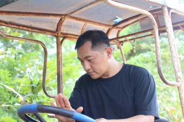 Odaklanmış bir adam kırsal bir aracı açık hava ortamında kullanıyor, yeşilliklerle çevrili bir tarım ortamında konsantrasyon ve çaba gösteriyor..