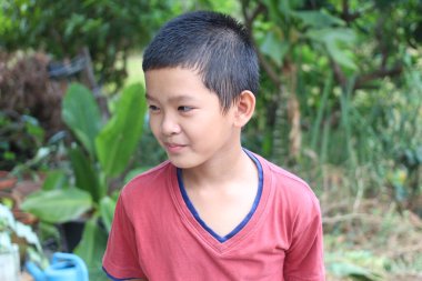 Neşeli genç bir çocuk yemyeşil yemliklerle çevrili açık havada bir anın tadını çıkarıyor. Gülüşü çocukluğun masumiyetini ve neşesini doğal bir ortamda yakalıyor..