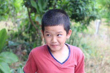 Neşeli bir çocuk neşeli bir ifadeyle yemyeşil bir ortamda duruyor, çocukluk sevincini ve doğanın güzelliğini samimi bir anda somutlaştırıyor..