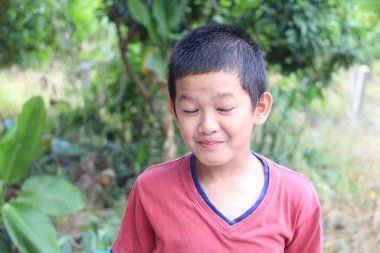 Doğanın güzelliğinin tadını çıkaran neşeli bir çocuk yemyeşil bir ortamda hafifçe gülümsüyor. Çocukluk sevincinin ve masumiyetin özünü yakalar..