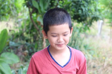 Neşeli genç bir çocuk yeşilliklerle çevrili, yemyeşil bir ortamda duruyor. Neşeli ifadesi, güneşli bir günde masumiyeti ve mutluluğu yansıtıyor..