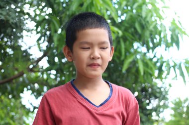 Genç bir çocuk yemyeşil bir çevrede durup düşünceli bir ifade sergiliyor. Sahne çocukluğun özünü ve doğadaki sükuneti yakalıyor..