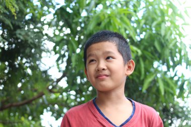 Düşünceli genç bir çocuk yemyeşil bir ortamda duruyor ve tuhaf bir ifade sergiliyor. Görüntü, çocukluk merakının ve doğadaki huzurun özünü yakalar..