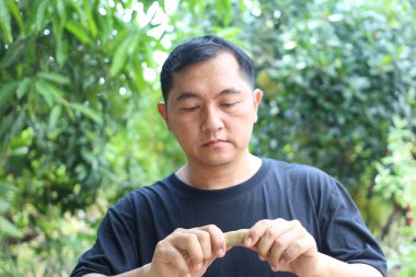 Bir adam yemyeşil bir nesneyle çevriliyken bir nesneyle etkileşime girer. Onun odaklanmış ifadesi ve sakin açık hava çevresi bir keşif ve merak hissi yaratıyor..