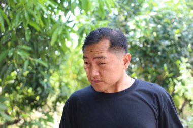 Düşünceli bir adam açık havada poz verir, yemyeşil ile çevrili, sakin bir doğal ortamda bir yansıma ve sükunet anı yakalar..