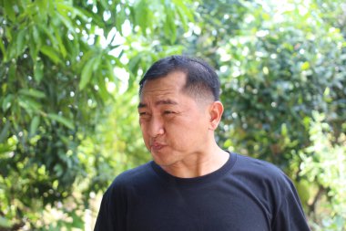 Düşünceli bir adam açık havada, yemyeşil bir ortamda, canlı doğal bir arka plana karşı sakin bir ifade sergiliyor. Yaşam tarzı temaları için mükemmel.