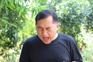 Yeşilliklerle çevrili açık havada güçlü bir duygu ifade eden bir adam. Samimi tepkisi, doğal bir ortamda anlık bir neşe ve doğallık yakalıyor..