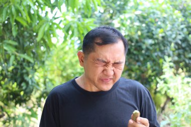 Dışarıdaki bir adam, yemyeşil bir arka planda değişik duygular gösteren alışılmadık bir besin maddesini tatmaya tepki veriyor. Onun ifadesi beklenmedik lezzetleri vurgular..