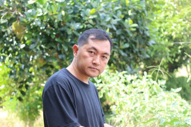 Dalgın bir adam yemyeşil bir ortamda dışarıda poz verir, sükunet ve sükunet hissini yansıtır. Sağlık ve doğa konuları için mükemmel..