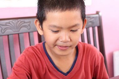 Genç bir çocuk içeride yaratıcı bir aktiviteyle uğraşırken konsantrasyonunu gösteriyor. Odaklanmış ifadesi çocukluk sevincinin ve merakının özünü yakalıyor..