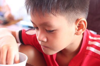 Kırmızı tişörtlü genç bir çocuk, çocukluk merakı ve neşesinin özünü canlı bir iç mekanda yakalamaya odaklanır..