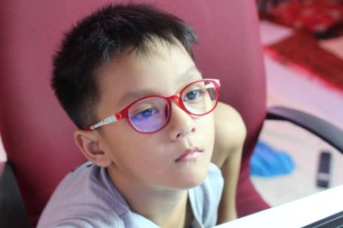 Kırmızı gözlüklü genç bir çocuk düşünceli bir şekilde oturur ve kameraya bakmaz. Onun sakin ifadesi modern bir kapalı mekan ortamında bir anlık tefekkür görüntüsü yakalıyor..