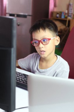 Gözlüklü genç bir çocuk rahat bir ofisteki bilgisayarın başında çalışıyor. Odaklanmış ifadesi teknoloji ve öğrenme ile bağlantısını gösteriyor..