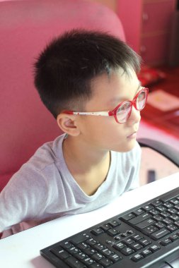 Gözlüklü odaklanmış genç bir çocuk bir bilgisayar masasında oturuyor, işine dalmış. Atmosferde öğrenme ve merak duygusu var..