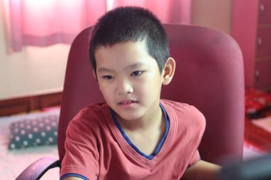 Derinden derslerine odaklanmış genç bir çocuk, parlak bir odada bir masada oturuyor. Onun ifadesi merakı ve bağlılığı yansıtıyor, öğrenmenin sevincini gösteriyor..