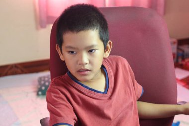 Genç bir çocuk, çocukluğunu duygusal bir şekilde yansıtan odaklanmış bir ifadeyle bir sandalyeye oturur. İçerideki hareketli ortam sahneye sıcaklık katıyor..