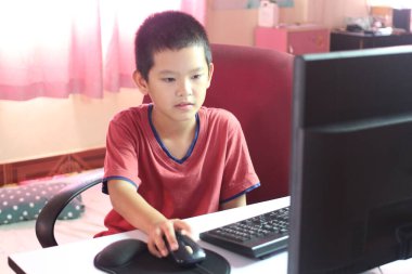 Genç bir çocuk rahat bir ev ortamında bilgisayar kullanmaktan hoşlanır. Ekrana odaklanıyor, teknolojinin ve çocukluk araştırmalarının birleştirilmesini gösteriyor..