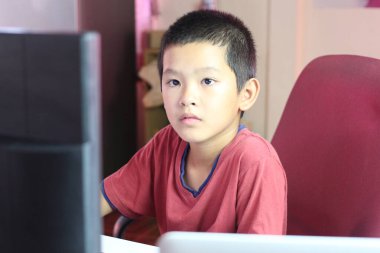 Genç bir çocuk masa başında oturur, dikkatle bilgisayar ekranına odaklanır, modern bir çalışma ortamında konsantrasyonunu gösterir..