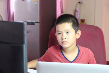 Genç bir çocuk ev ortamında bilgisayar ekranına bağlanır, ev ödevlerini öğrenirken veya tamamlarken odak ve konsantrasyon gösterir.