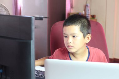 Genç bir çocuk bilgisayar ekranı ile meşgul bir şekilde bir masada dikkatle oturur. Bir anlık bir konsantrasyon yakalayarak, dijital dünyayı ev ortamında keşfeder..