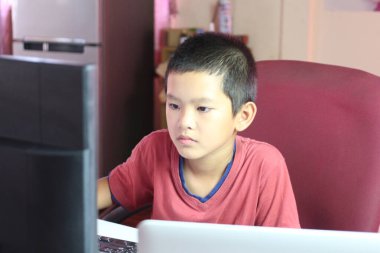 Genç bir çocuk bilgisayar ekranına odaklanmış bir şekilde bir masada oturuyor. Bu görüntü, çocukluk ilişkisinin özünü bir ev ortamında teknolojiyle yakalıyor..