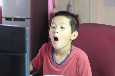 Genç bir çocuk evde bilgisayar kullanırken şaşırmış bir ifade sergiliyor. Teknolojiye olan bağlılığı gelişigüzel bir ortamda merak ve heyecanı vurguluyor..