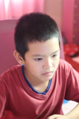 Ev masasında oturan, bilgisayarla meşgul odaklı bir çocuk. Ciddi bir yüz ifadesi sergiliyor, ev ortamında konsantrasyonu vurguluyor..