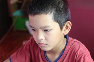 Kırmızı gömlekli genç bir çocuk işine dikkatle odaklanırken ciddi bir yüz ifadesi sergiliyor. Bu samimi kapalı mekan sahnesi çocukluk konsantrasyonunun ve nişanlanmanın özünü yakalar..