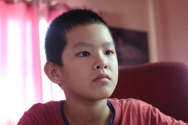 Ciddi bir ifadeye sahip genç bir çocuk evde oturur ve bir anlık tefekküre kapılır. Doğal ışık ve basit arka plan, onun düşünceli davranışlarını vurguluyor..