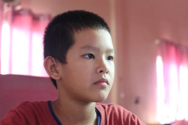 Ciddi bir ifadeye sahip genç bir çocuk kapalı alanda bilgisayar kullanmaya yoğunlaşır. Odaklanmış tavrı, eğitimin ya da eğlencenin bir parçası olduğunu gösteriyor..