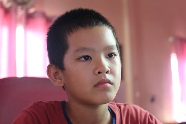 Odaklanmış genç bir çocuk içeride oturur, derin bir konsantrasyon ve ciddiyet gösterir. Düşünceli ifadesi, günlük ev ortamında öğrenme ve bağlanma anını yakalıyor..