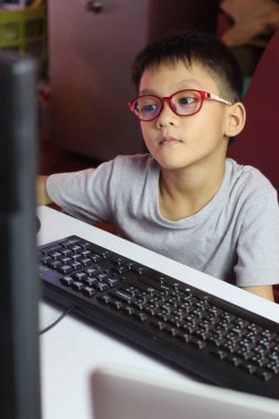 Gözlük takan genç bir çocuk evde çalışırken bir bilgisayar ekranına odaklanır. Bu görüntü, çocuklar için modern eğitim ve teknolojinin özünü yansıtır..
