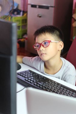 Gözlük takan genç bir çocuk dikkatle evdeki bilgisayar ekranına odaklanıyor, modern bir öğrenme ortamında bir anlık konsantrasyon ve merak gösteriyor..