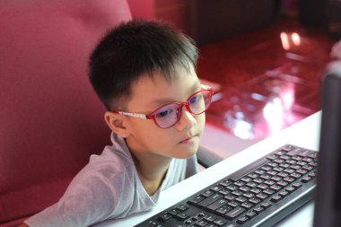 Gözlük takan genç bir çocuk dikkatle bilgisayar ekranına odaklanıyor. Sahne, merakın özünü ve modern bir çevrede öğrenmenin neşesini yakalıyor..