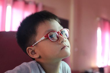 Gözlüklü genç bir çocuk düşünceli bir şekilde pembe bir arka plana bakıyor. Bu resim, eğitici temalar için ideal olan merak ve konsantrasyonu yakalar.