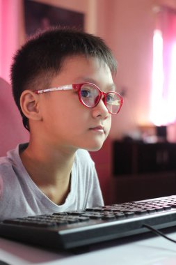 Gözlüklü genç çocuk dikkatle bilgisayar ekranına odaklanıyor. Bir merak ve çatışma anını yakalayan bu görüntü gençliği ve teknolojiyi vurguluyor..