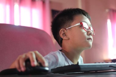 Gözlük takan genç bir çocuk ekranda odaklanmış bir bilgisayara dikkatle oturur. Görüntü, dijital çağda konsantrasyonu ve çocukluğun özünü yakalar..