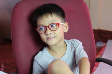 Gözlüklü neşeli bir çocuk sandalyede rahatça oturur ve düşünceli bir ifade sergiler. İçerideki ortam çocukluk sevincini ve merakını yakalıyor..