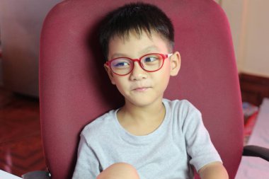 Gözlük takan genç bir çocuk sıcak bir odada düşünceli bir şekilde oturur. Cazibesi ve masumiyeti yayar. Yumuşak ışık, onun neşeli ama ciddi ifadesini arttırır. Çeşitli temalar için mükemmeldir..