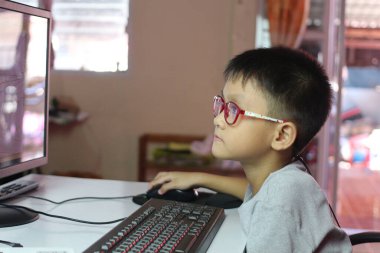 Gözlük takan genç bir çocuk bir bilgisayar ekranı ile derinden meşgul bir şekilde masada oturuyor. Görüntü onun konsantrasyonunu ve merakını modern bir öğrenme ortamında yakalıyor..