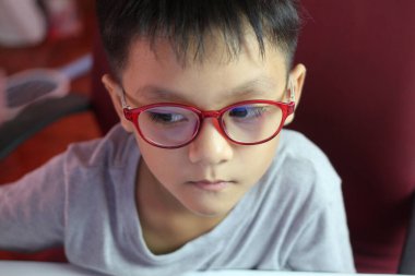 Kırmızı gözlük takan genç bir çocuk bir göreve derinden odaklanır. İfadesi, iç mekandaki konsantrasyon ve merakı yansıtıyor. Eğitici temalar için mükemmel..