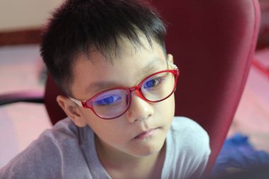 Kırmızı gözlük takan düşünceli bir çocuğun yakın plan portresi evde otururken ciddi bir tavır sergiliyor. Eğitim ve gençlik temaları için mükemmel.