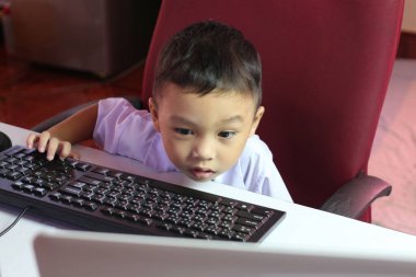 Genç bir çocuk ilginç bir şekilde bir bilgisayar ekranını inceliyor, ev ortamında ilgi ve merak gösteriyor. Modern çocukluk keşiflerinin ve öğrenmenin bir fotoğrafı..