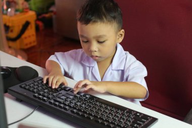 Genç bir çocuk yoğun bir şekilde klavyeye yazmaya odaklanmış, evde çalışma ortamında teknolojiyle ilgili merak ve bağlılık sergiliyor.